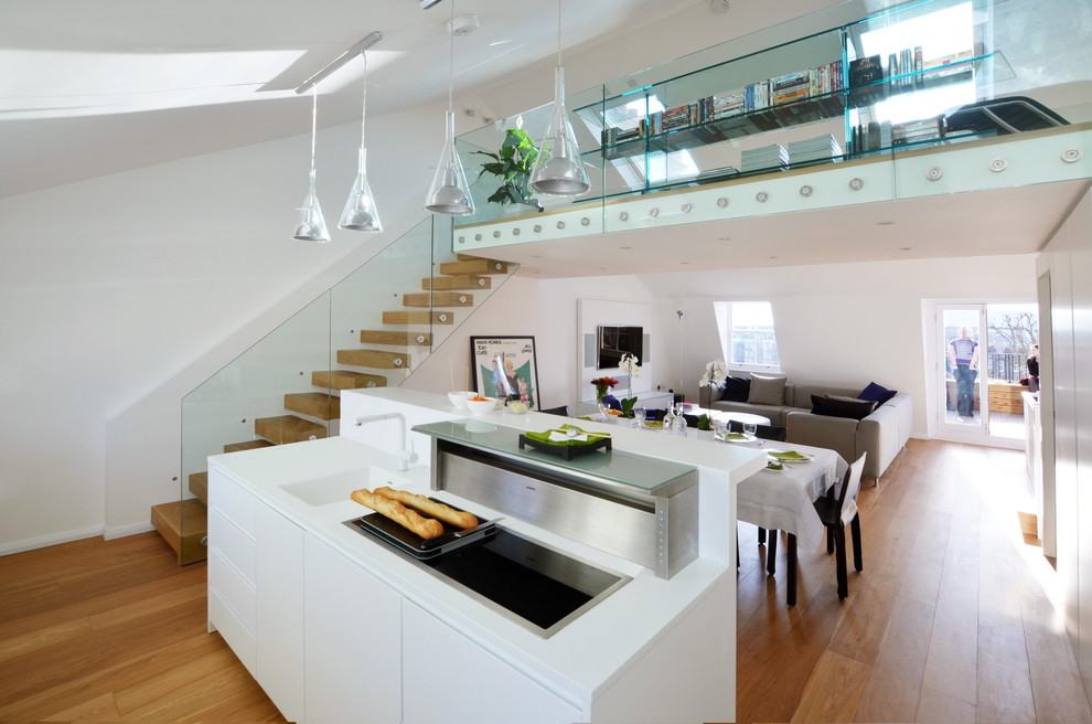 Photo of a mid-sized contemporary open plan kitchen in London with a drop-in sink, flat-panel cabinets, white cabinets, solid surface benchtops, white splashback, stainless steel appliances, with island, white benchtop, light hardwood floors and beige floor.