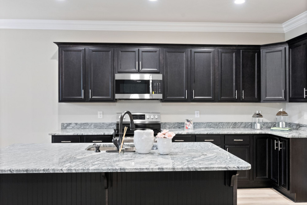 Mid-sized elegant l-shaped brown floor eat-in kitchen photo with a drop-in sink, black cabinets, granite countertops, stainless steel appliances, an island and white countertops