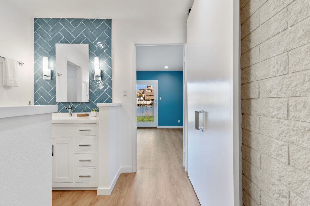 This is an example of a large beach style master bathroom in San Francisco with shaker cabinets, white cabinets, blue tile, ceramic tile, solid surface benchtops, white benchtops, a double vanity, a built-in vanity, white walls, light hardwood floors, an integrated sink and brown floor.