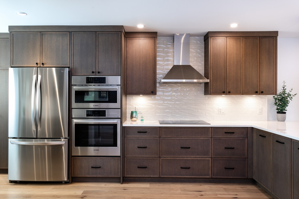 Open concept kitchen - mid-sized transitional u-shaped medium tone wood floor and brown floor open concept kitchen idea in Vancouver with an undermount sink, shaker cabinets, dark wood cabinets, quartz countertops, white backsplash, porcelain backsplash, stainless steel appliances, a peninsula and white countertops