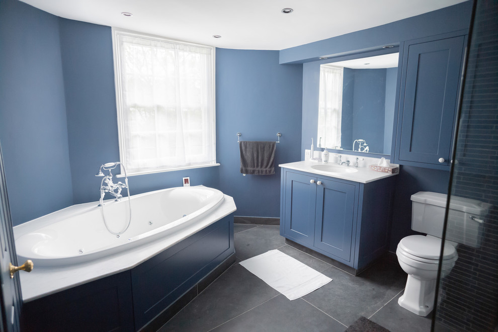 Large contemporary kids bathroom in London with shaker cabinets, blue cabinets, a corner tub, an open shower, a two-piece toilet, black tile, slate, blue walls, slate floors, an undermount sink, marble benchtops, grey floor, an open shower and white benchtops.