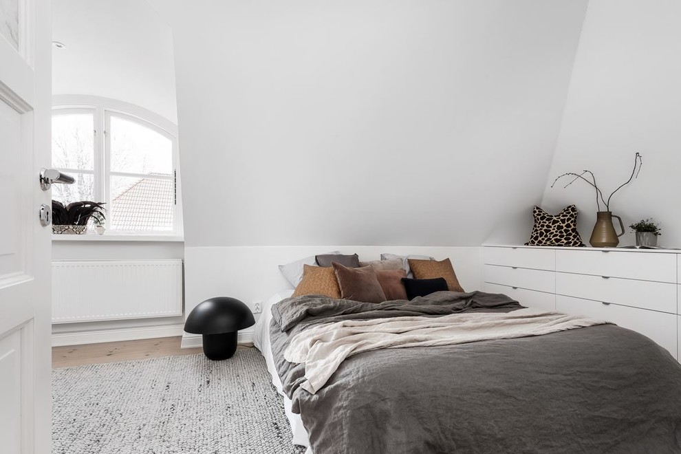 Small scandinavian bedroom in Stockholm with white walls, no fireplace, light hardwood floors and brown floor.