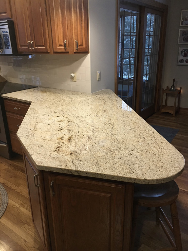 Eat-in kitchen - large transitional u-shaped medium tone wood floor eat-in kitchen idea with an undermount sink, raised-panel cabinets, medium tone wood cabinets, granite countertops, white backsplash, ceramic backsplash, stainless steel appliances and an island