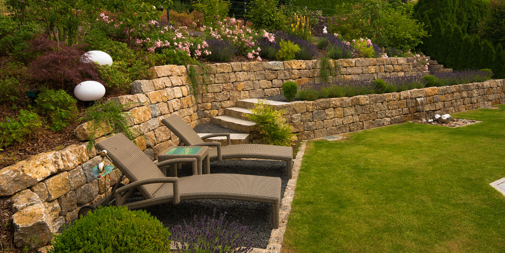 Photo of a large traditional sloped full sun garden for summer in Frankfurt with a retaining wall and natural stone pavers.