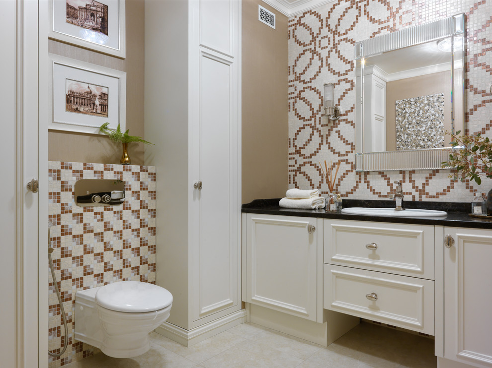 Design ideas for a transitional powder room in Moscow with recessed-panel cabinets, a wall-mount toilet, mosaic tile, a drop-in sink, beige floor, black benchtops, beige cabinets, multi-coloured tile and brown walls.