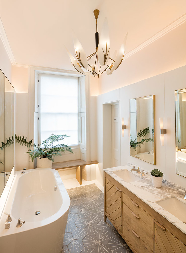This is an example of a mid-sized traditional master bathroom in London with flat-panel cabinets, medium wood cabinets, a freestanding tub, gray tile, white walls, a drop-in sink and marble benchtops.