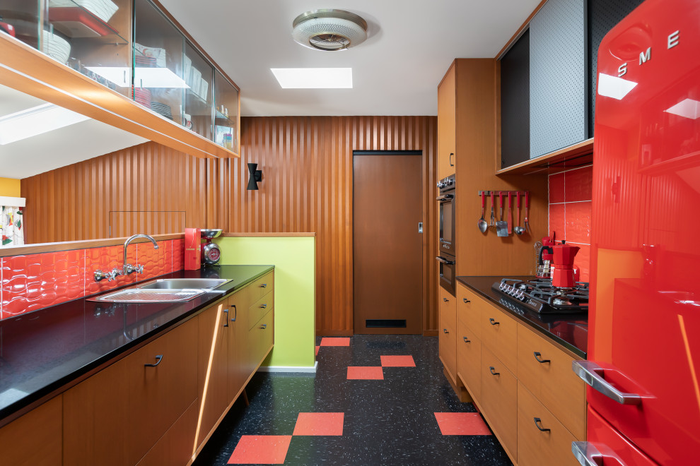 Photo of a mid-sized midcentury galley separate kitchen in Melbourne with a single-bowl sink, ceramic splashback, black appliances, multi-coloured floor and red splashback.