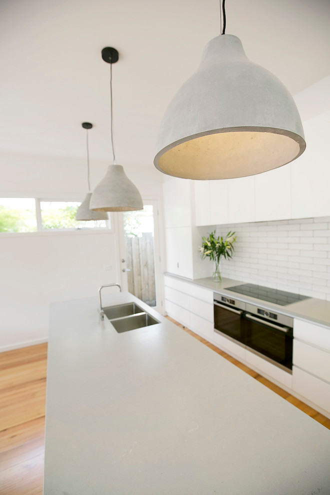 Contemporary kitchen in Melbourne with a double-bowl sink, white cabinets, quartz benchtops, white splashback, ceramic splashback, black appliances, light hardwood floors and with island.