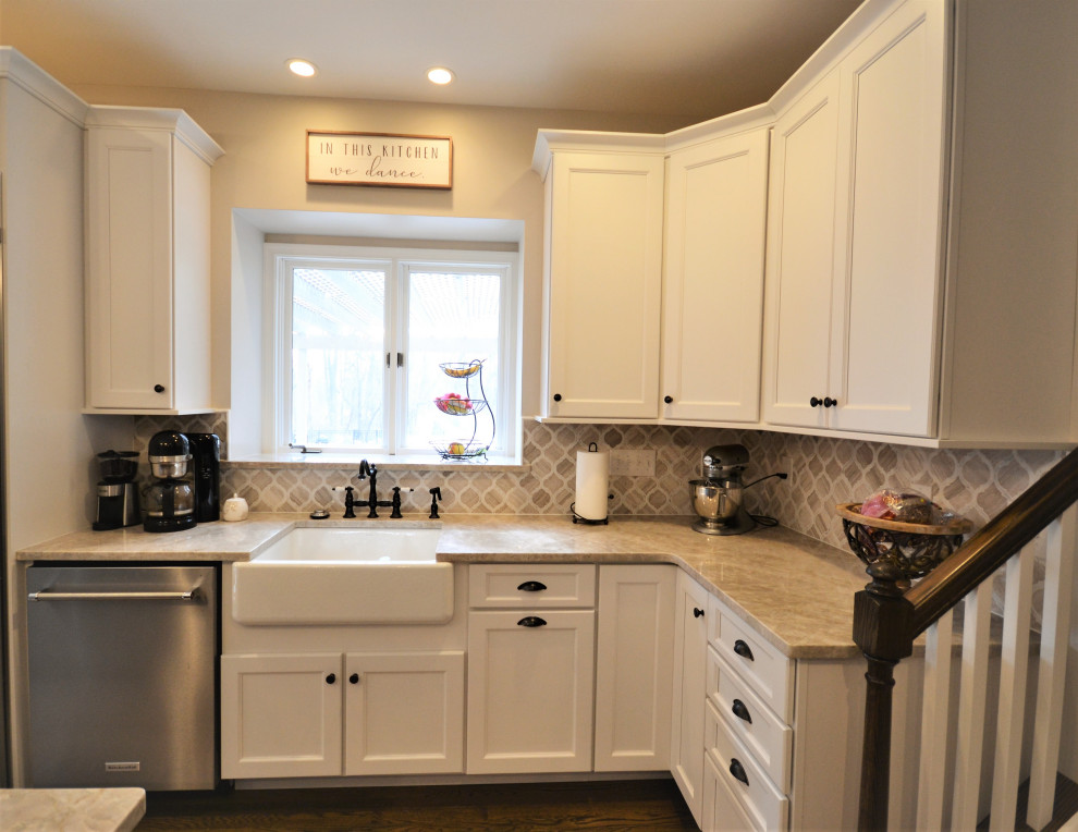 This is an example of a large transitional u-shaped eat-in kitchen in Philadelphia with a farmhouse sink, raised-panel cabinets, white cabinets, quartzite benchtops, beige splashback, marble splashback, stainless steel appliances, medium hardwood floors, with island, brown floor and beige benchtop.
