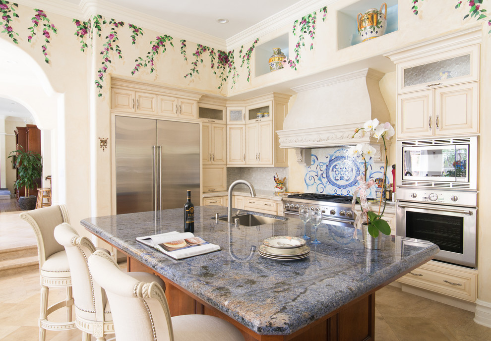 Photo of a large mediterranean l-shaped eat-in kitchen in Los Angeles with an undermount sink, raised-panel cabinets, beige cabinets, granite benchtops, grey splashback, matchstick tile splashback, stainless steel appliances, porcelain floors and with island.