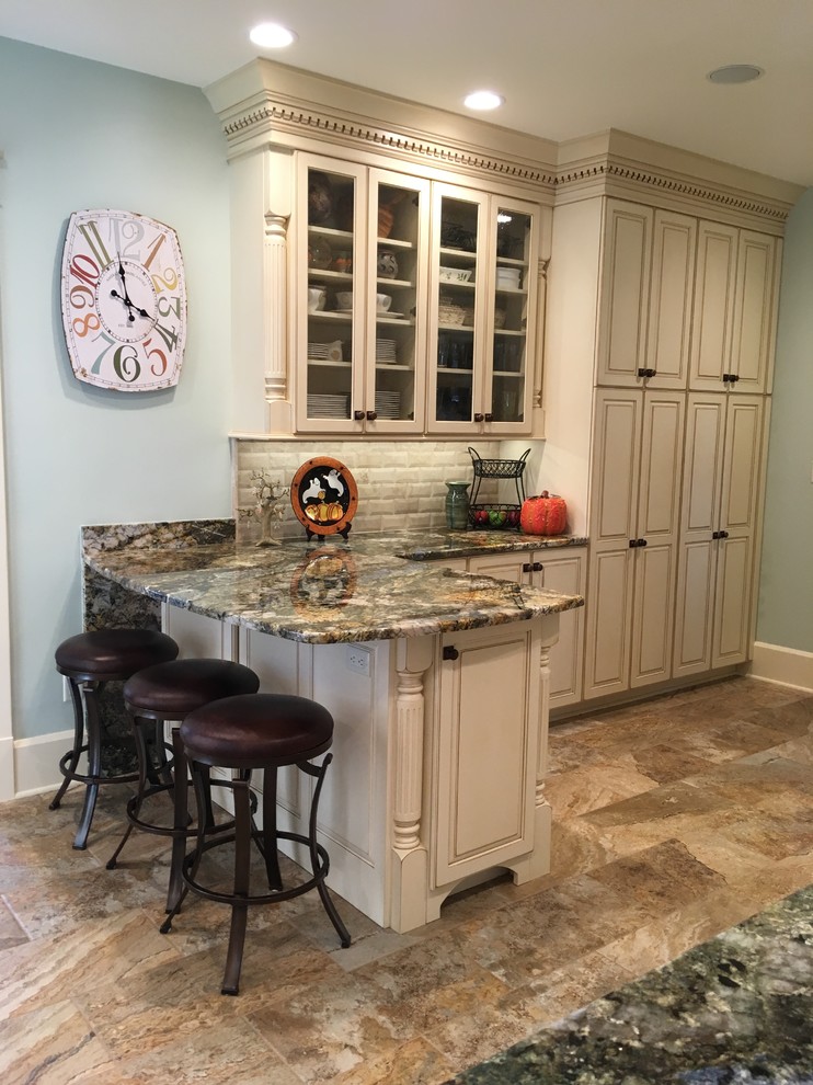 Inspiration for a large transitional galley porcelain tile enclosed kitchen remodel with an undermount sink, raised-panel cabinets, distressed cabinets, granite countertops, beige backsplash, stone tile backsplash, stainless steel appliances and a peninsula