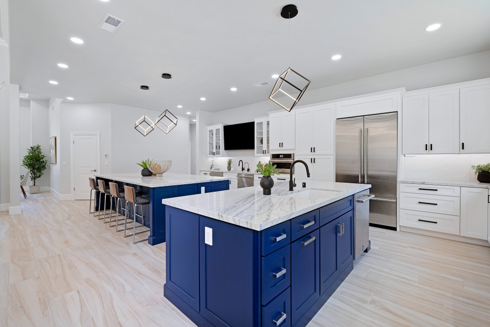 Design ideas for an expansive contemporary l-shaped open plan kitchen in Other with a single-bowl sink, shaker cabinets, blue cabinets, quartzite benchtops, white splashback, porcelain splashback, stainless steel appliances, porcelain floors, multiple islands, beige floor and white benchtop.