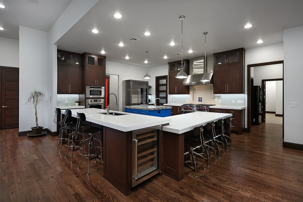 Large modern u-shaped eat-in kitchen in Oklahoma City with a drop-in sink, shaker cabinets, dark wood cabinets, quartz benchtops, white splashback, stainless steel appliances, medium hardwood floors, with island and brown floor.