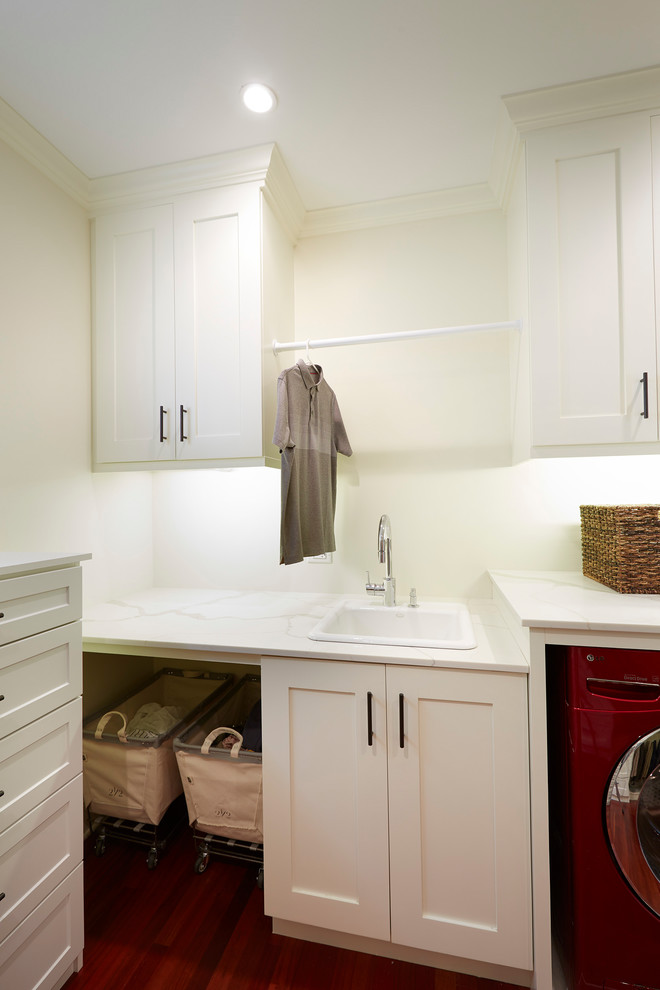 This is an example of a mid-sized arts and crafts single-wall utility room in Chicago with a drop-in sink, shaker cabinets, white cabinets, quartz benchtops, white walls, dark hardwood floors, a side-by-side washer and dryer, red floor and white benchtop.