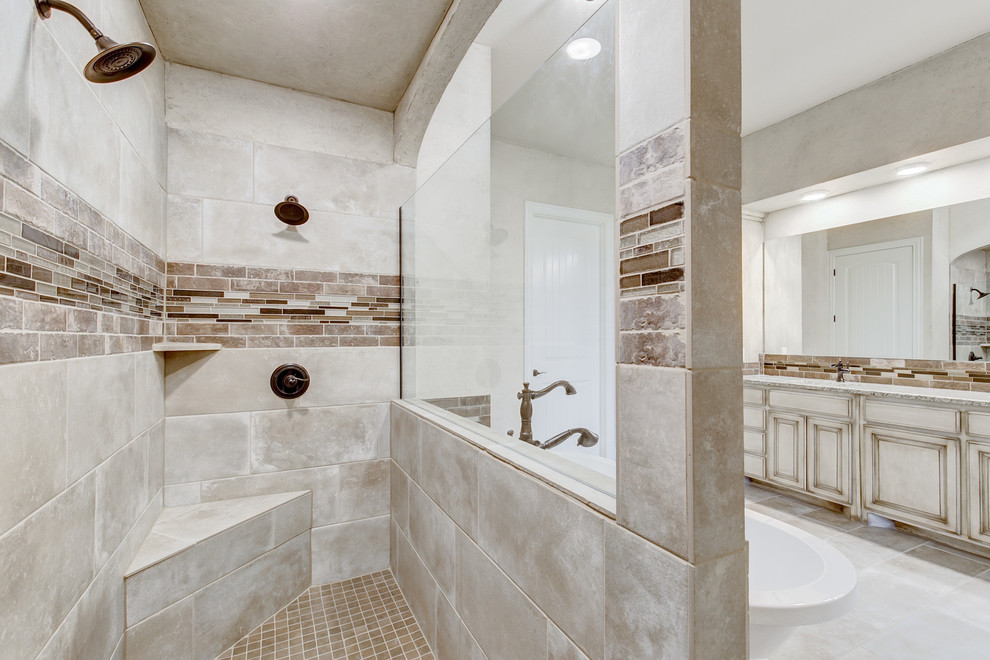 Design ideas for a large mediterranean master bathroom in Dallas with raised-panel cabinets, distressed cabinets, a freestanding tub, a double shower, brown tile, matchstick tile, beige walls, an undermount sink, granite benchtops, grey floor, an open shower and beige benchtops.