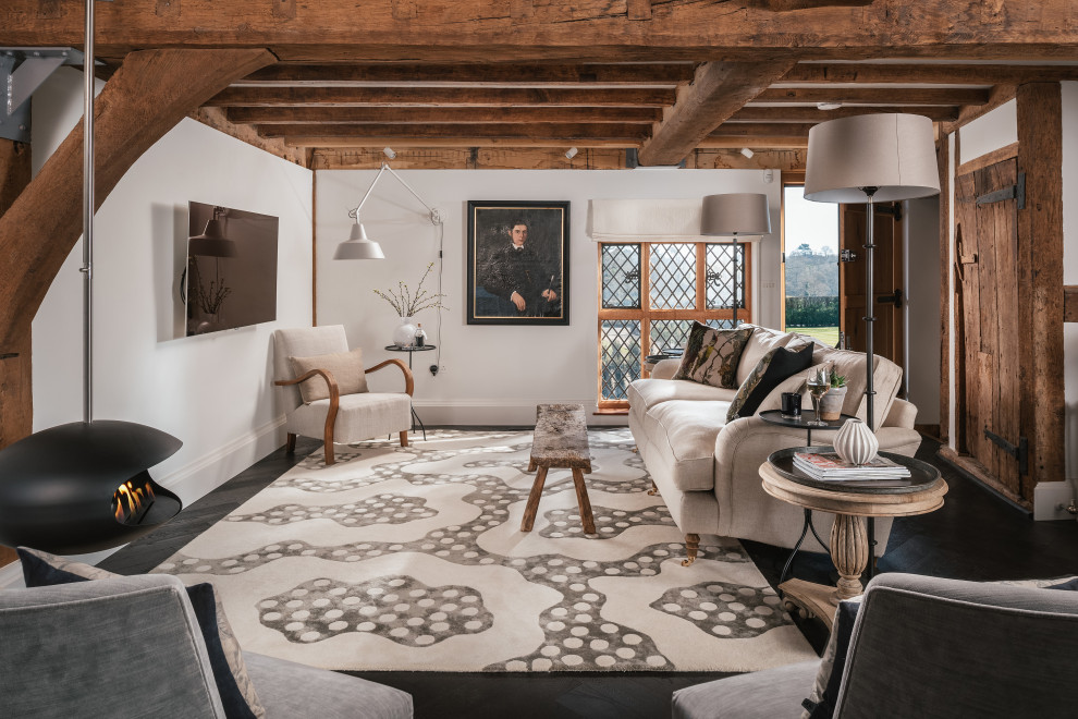 Design ideas for a medium sized rural games room in Sussex with white walls, dark hardwood flooring, a hanging fireplace, a wall mounted tv, black floors and exposed beams.