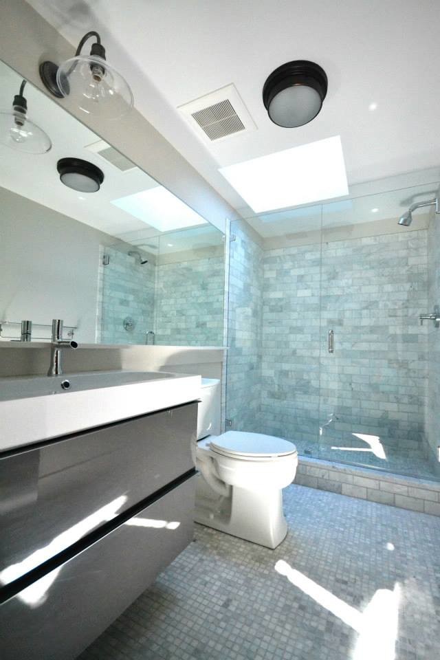 This is an example of a large contemporary master bathroom in Portland Maine with gray tile, grey walls, mosaic tile floors, flat-panel cabinets, grey cabinets, marble, solid surface benchtops, white benchtops, an alcove tub, an alcove shower, a two-piece toilet, a trough sink, white floor and a hinged shower door.