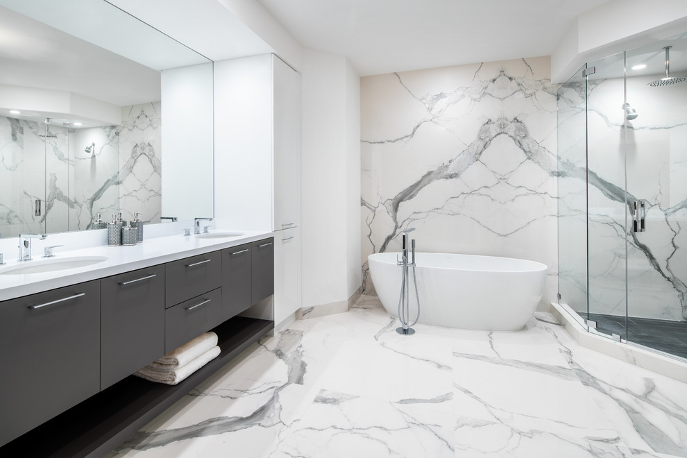 Large contemporary master bathroom in Miami with flat-panel cabinets, grey cabinets, a freestanding tub, a corner shower, a one-piece toilet, white tile, porcelain tile, white walls, porcelain floors, an undermount sink, engineered quartz benchtops, white floor, a hinged shower door and white benchtops.