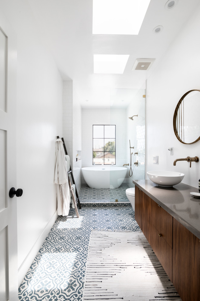 Inspiration for a mid-sized mediterranean master bathroom in Los Angeles with flat-panel cabinets, brown cabinets, a freestanding tub, a shower/bathtub combo, a wall-mount toilet, white tile, ceramic tile, white walls, ceramic floors, a vessel sink, engineered quartz benchtops, blue floor, a hinged shower door, grey benchtops, a double vanity and a floating vanity.