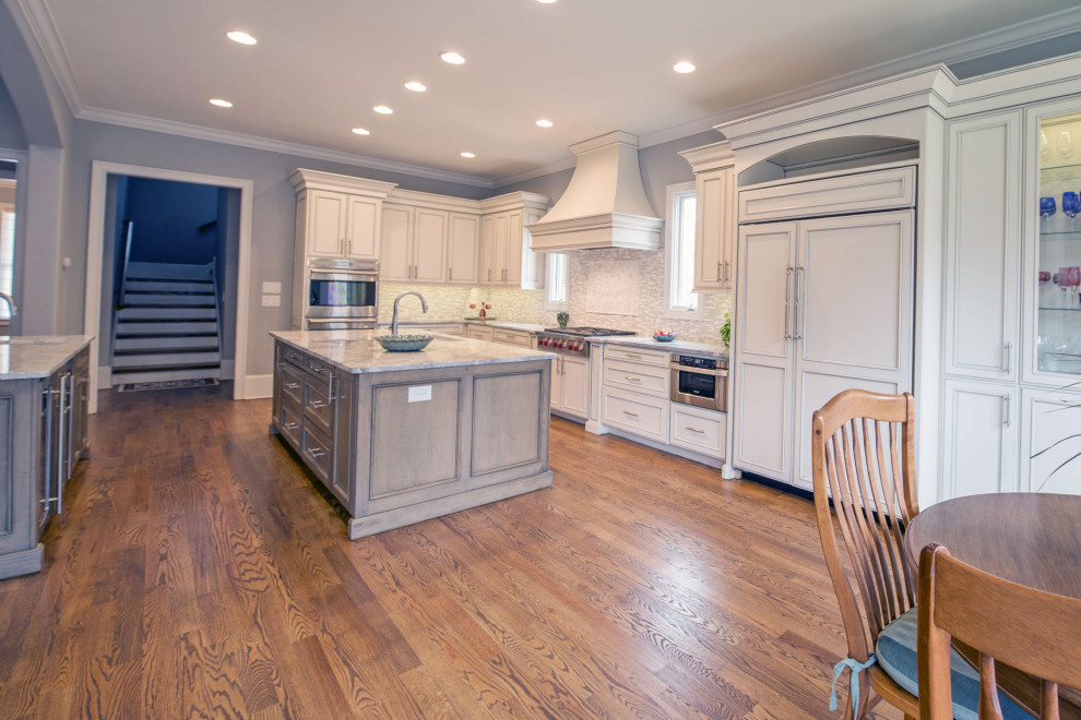 Inspiration for a large transitional l-shaped medium tone wood floor and brown floor eat-in kitchen remodel with an undermount sink, gray backsplash, stainless steel appliances, two islands, beige cabinets, marble countertops and glass tile backsplash