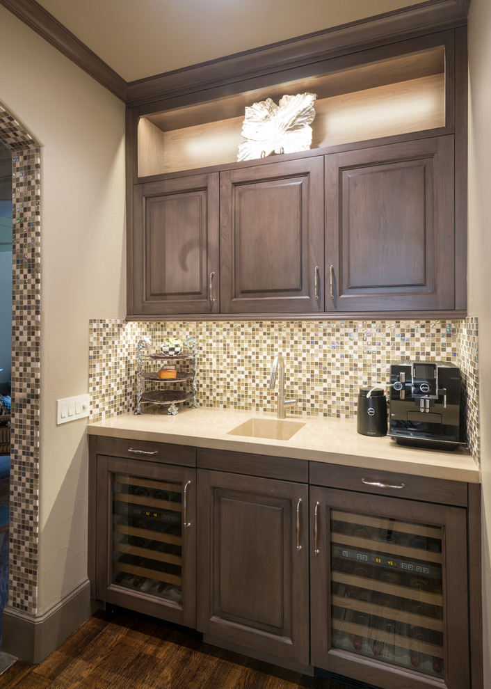 This is an example of a small traditional single-wall wet bar in Dallas with an integrated sink, raised-panel cabinets, medium wood cabinets, concrete benchtops, multi-coloured splashback, mosaic tile splashback and medium hardwood floors.