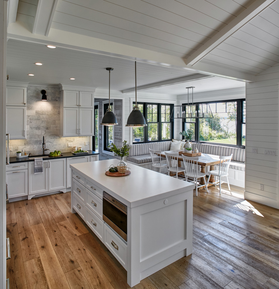 Photo of a mid-sized beach style l-shaped eat-in kitchen in Grand Rapids with an undermount sink, shaker cabinets, white cabinets, quartz benchtops, white splashback, marble splashback, stainless steel appliances, light hardwood floors, with island, beige floor and white benchtop.
