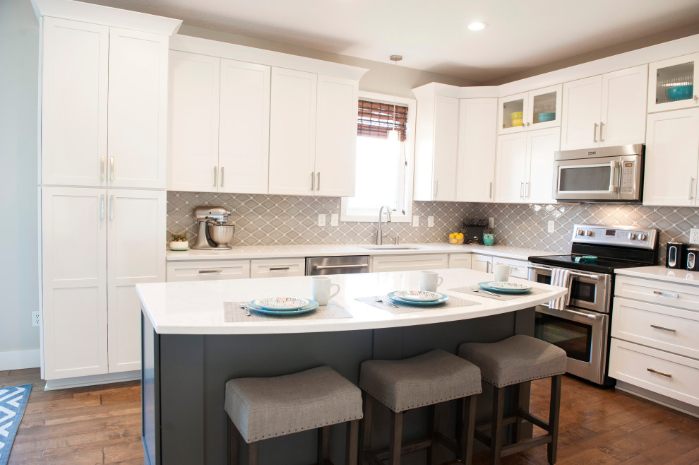 Mid-sized transitional l-shaped medium tone wood floor and brown floor eat-in kitchen photo with an undermount sink, shaker cabinets, white cabinets, quartz countertops, gray backsplash, mosaic tile backsplash, stainless steel appliances, an island and white countertops