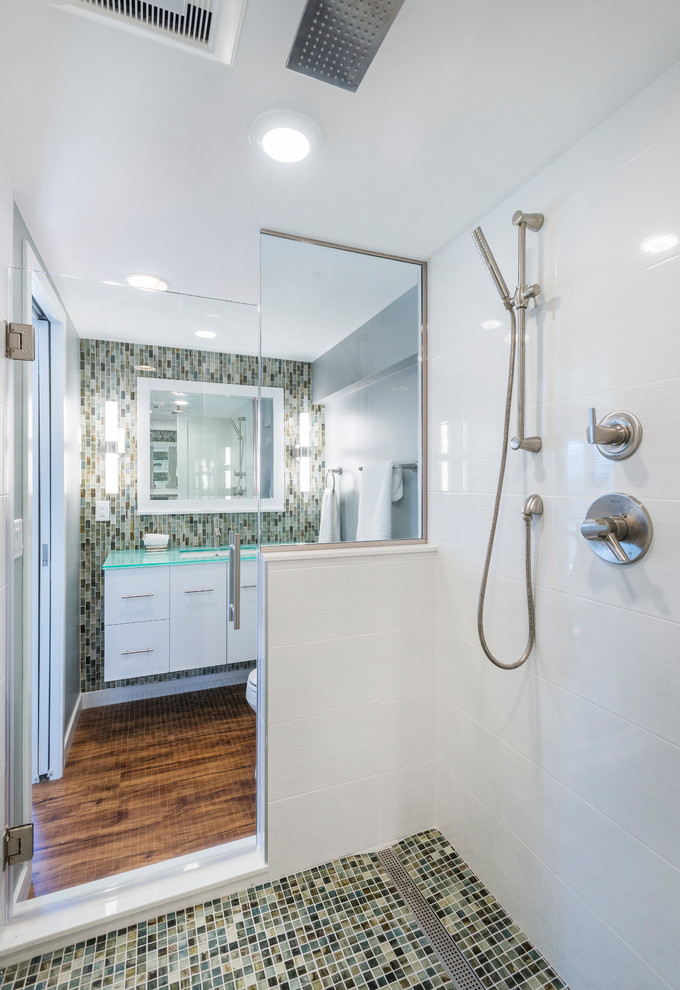 Inspiration for a small contemporary master wet room bathroom in Other with flat-panel cabinets, white cabinets, a two-piece toilet, multi-coloured tile, porcelain tile, grey walls, laminate floors, an undermount sink, glass benchtops, brown floor and a hinged shower door.