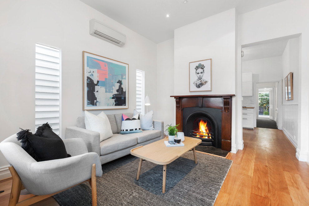 Transitional open concept living room in Melbourne with white walls, medium hardwood floors and a standard fireplace.