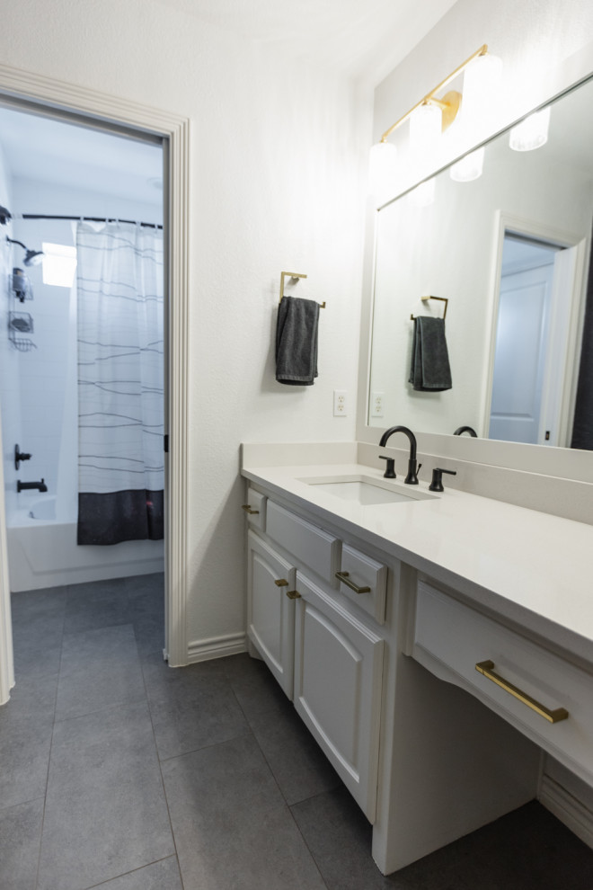 Photo of a mid-sized transitional kids bathroom in Dallas with raised-panel cabinets, white cabinets, a drop-in tub, a shower/bathtub combo, a one-piece toilet, white tile, porcelain tile, black walls, porcelain floors, an undermount sink, engineered quartz benchtops, grey floor, a shower curtain, white benchtops, a single vanity and a built-in vanity.