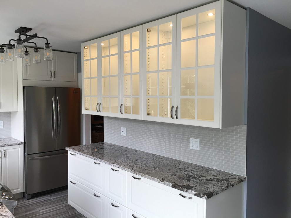 Photo of a mid-sized country u-shaped eat-in kitchen in Ottawa with a farmhouse sink, raised-panel cabinets, white cabinets, granite benchtops, beige splashback, glass tile splashback, stainless steel appliances, porcelain floors, no island and grey floor.