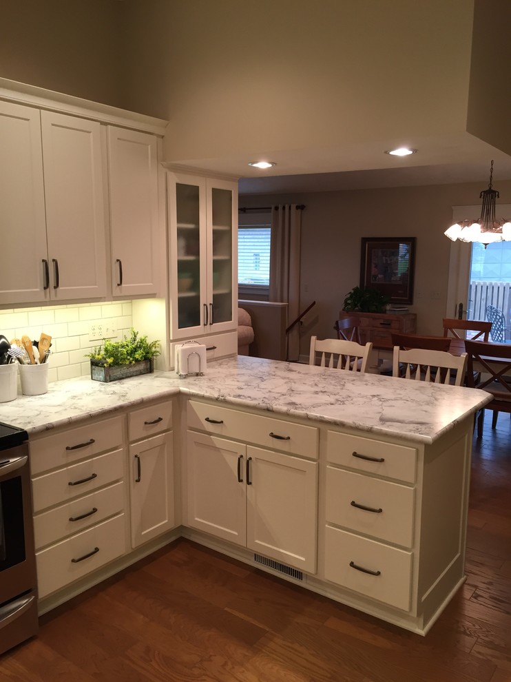 Mid-sized transitional u-shaped medium tone wood floor eat-in kitchen photo with an integrated sink, shaker cabinets, white cabinets, laminate countertops, white backsplash, subway tile backsplash, stainless steel appliances and a peninsula