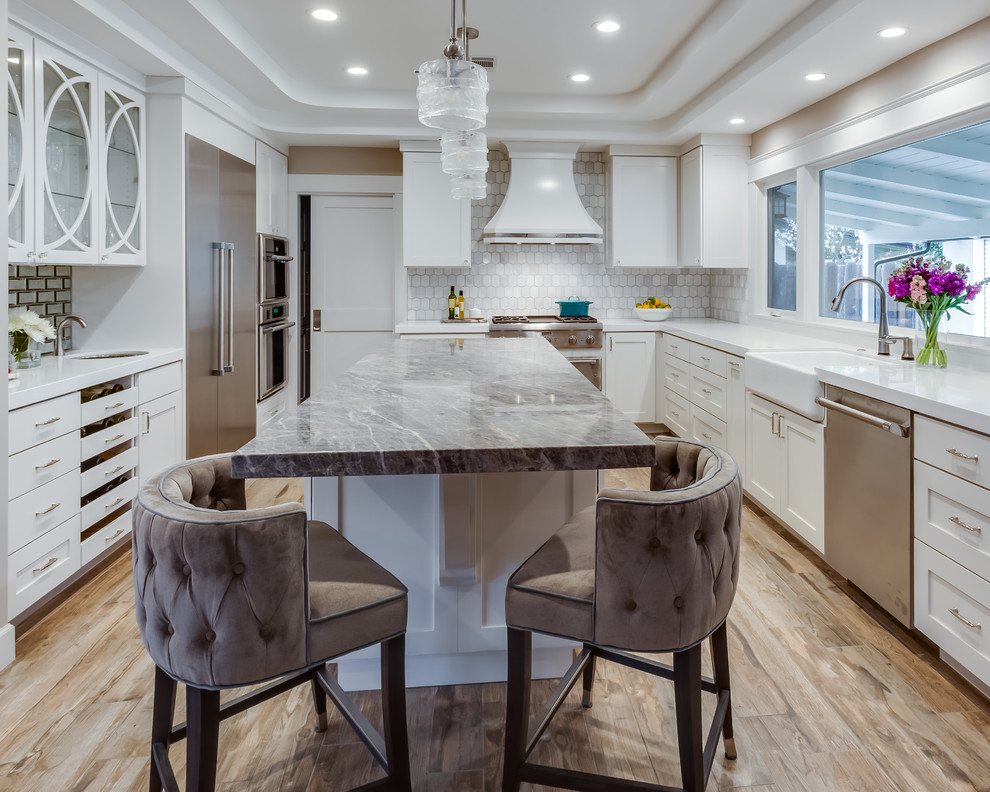 This is an example of a large transitional u-shaped separate kitchen in Sacramento with a farmhouse sink, shaker cabinets, white cabinets, quartzite benchtops, grey splashback, marble splashback, stainless steel appliances, with island, brown floor, white benchtop and porcelain floors.
