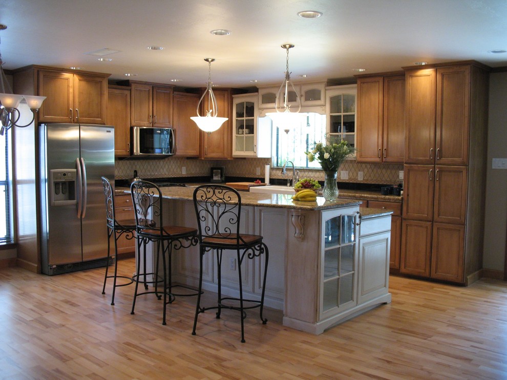 Example of a mid-sized l-shaped light wood floor eat-in kitchen design in Albuquerque with a farmhouse sink, raised-panel cabinets, medium tone wood cabinets, granite countertops, beige backsplash, stone tile backsplash, stainless steel appliances and an island