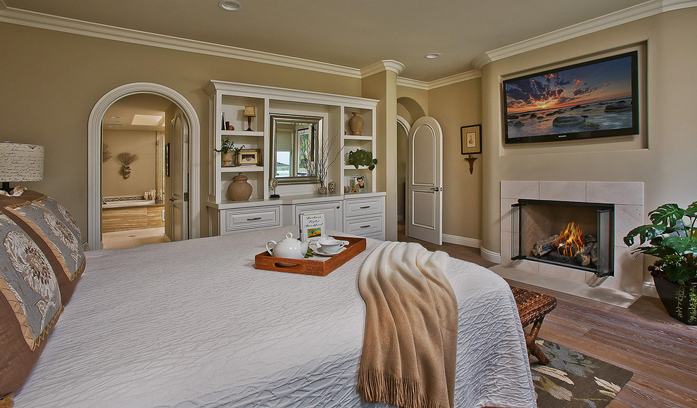 Large beach style master bedroom in Orange County with beige walls, medium hardwood floors, a standard fireplace and a stone fireplace surround.