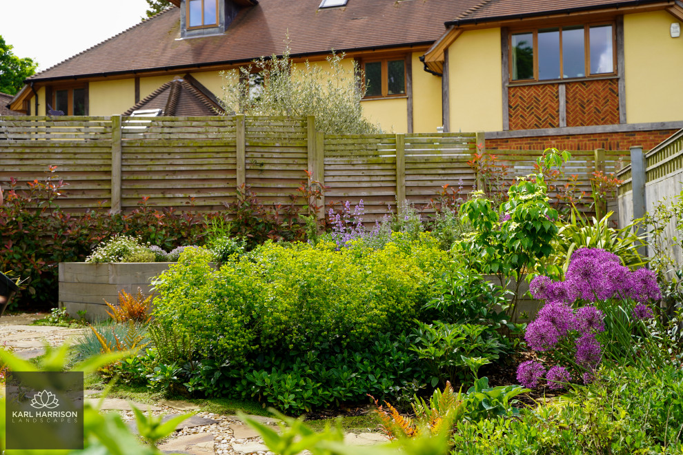 На фото: солнечный, летний регулярный сад среднего размера на заднем дворе в скандинавском стиле с клумбами, хорошей освещенностью, настилом и с деревянным забором