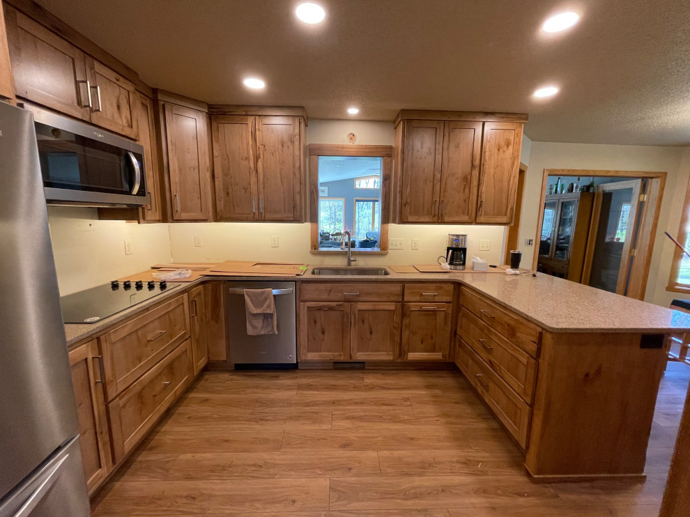 Light wood floor eat-in kitchen photo with an undermount sink, shaker cabinets, medium tone wood cabinets, stainless steel appliances, a peninsula and multicolored countertops