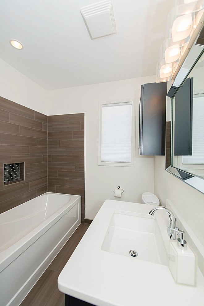 Photo of a small contemporary bathroom in Other with an undermount sink, recessed-panel cabinets, dark wood cabinets, engineered quartz benchtops, an alcove tub, a one-piece toilet, brown tile, porcelain tile, white walls and porcelain floors.