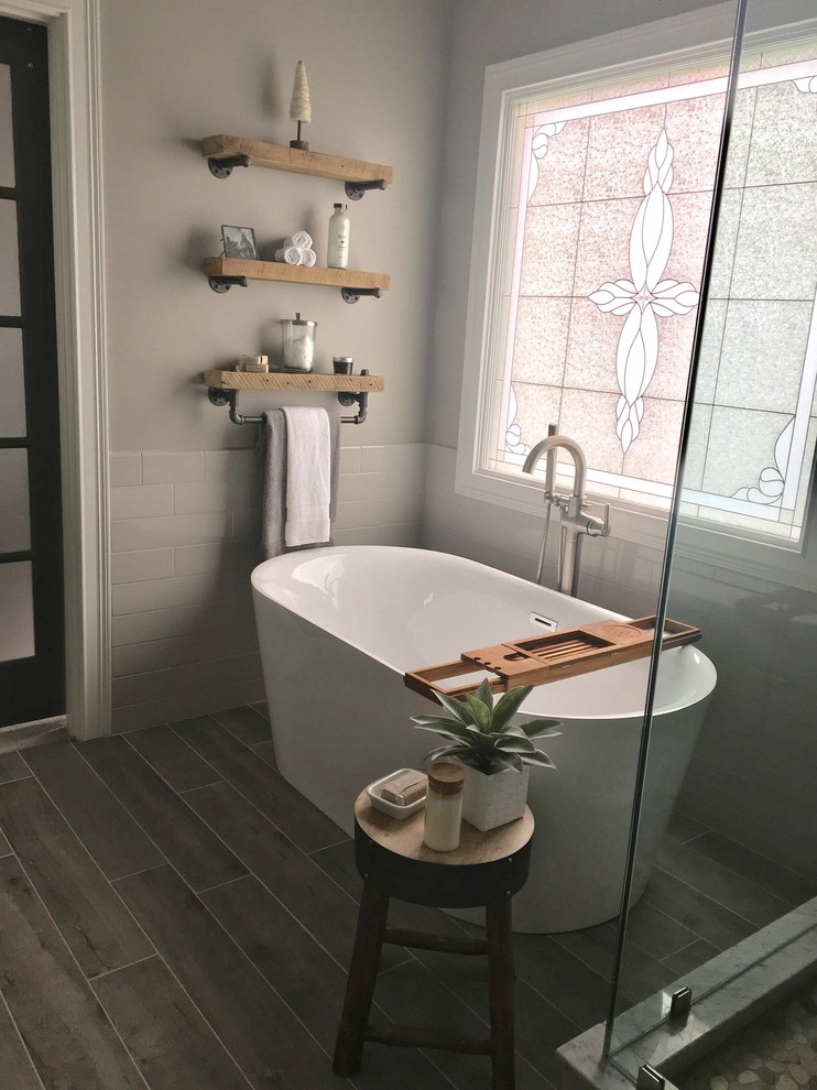 Freestanding bathtub - mid-sized transitional master subway tile and white tile laminate floor and gray floor freestanding bathtub idea with a one-piece toilet, gray walls, shaker cabinets, gray cabinets, a hinged shower door and a vessel sink