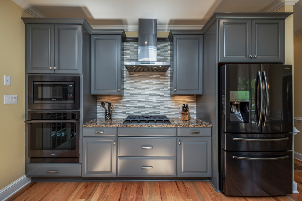 Inspiration for a transitional kitchen remodel with raised-panel cabinets, gray cabinets, granite countertops, black appliances, a peninsula and multicolored countertops