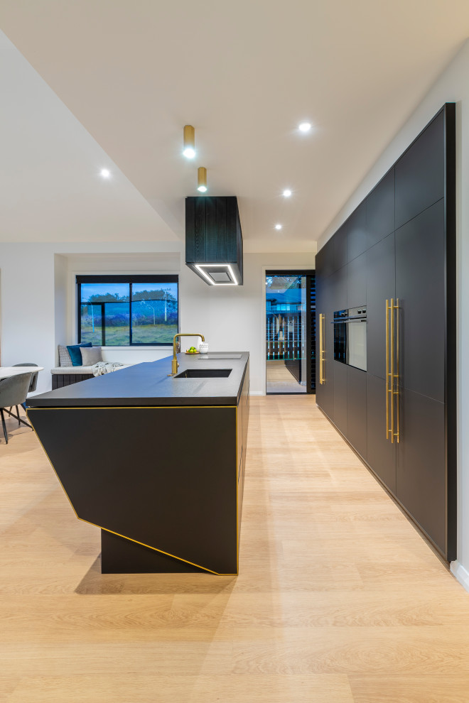Inspiration for a large contemporary galley open plan kitchen in Auckland with an undermount sink, black cabinets, black appliances, laminate floors, with island and black benchtop.