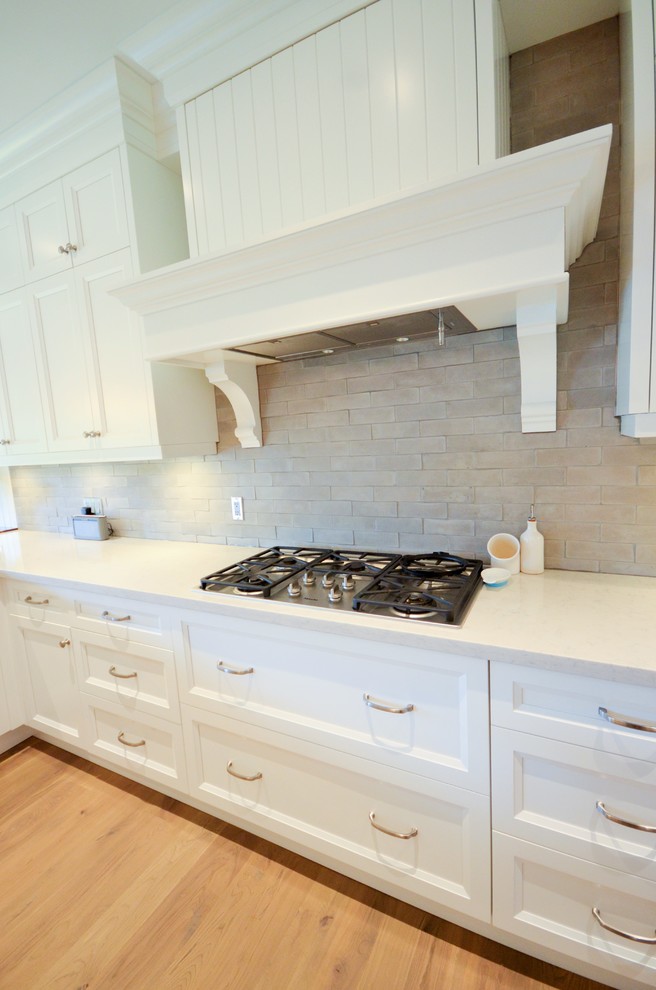 Photo of a large contemporary l-shaped open plan kitchen in Toronto with a farmhouse sink, shaker cabinets, white cabinets, granite benchtops, grey splashback, subway tile splashback, stainless steel appliances, light hardwood floors and multiple islands.