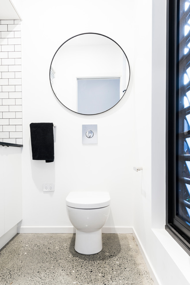 This is an example of a small contemporary powder room in Sydney with flat-panel cabinets, white cabinets, a one-piece toilet, white tile, subway tile, white walls, concrete floors, an undermount sink and black benchtops.
