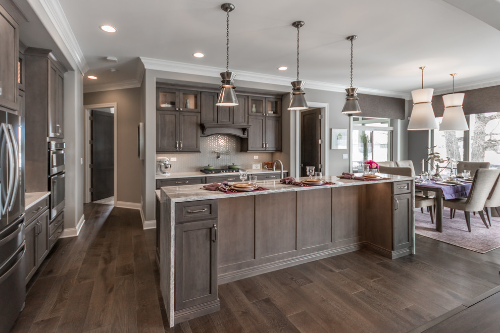 Mid-sized traditional eat-in kitchen in Chicago with a farmhouse sink, flat-panel cabinets, dark wood cabinets, quartz benchtops, beige splashback, glass tile splashback, stainless steel appliances, dark hardwood floors, with island, brown floor and white benchtop.