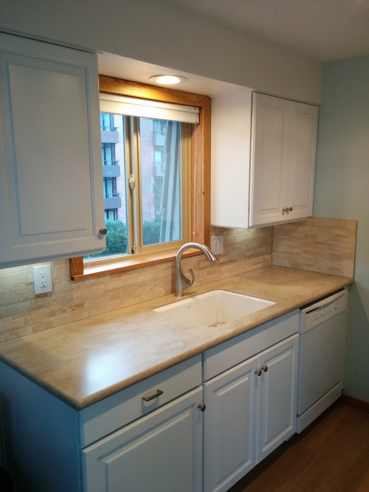 Photo of a small transitional galley separate kitchen in Seattle with an undermount sink, raised-panel cabinets, white cabinets, solid surface benchtops, beige splashback, stone tile splashback, white appliances, porcelain floors and no island.