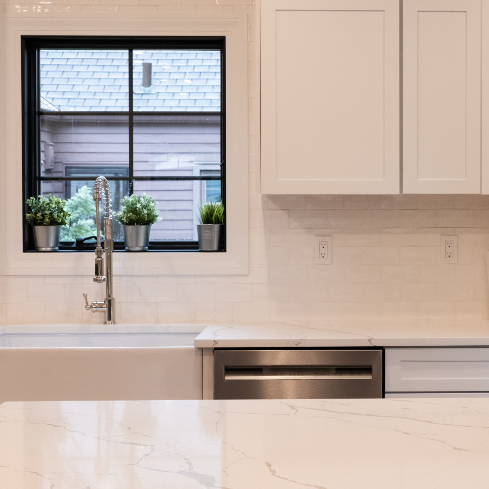 Mid-sized country l-shaped eat-in kitchen in New York with a farmhouse sink, shaker cabinets, white cabinets, quartz benchtops, white splashback, ceramic splashback, stainless steel appliances, light hardwood floors, with island and white benchtop.