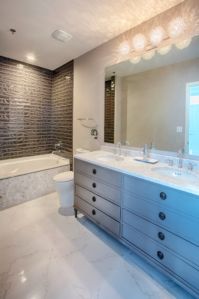 This is an example of a mid-sized contemporary master bathroom in Nashville with a drop-in sink, furniture-like cabinets, medium wood cabinets, marble benchtops, an alcove tub, a corner shower, a one-piece toilet, black tile, ceramic tile, beige walls and marble floors.