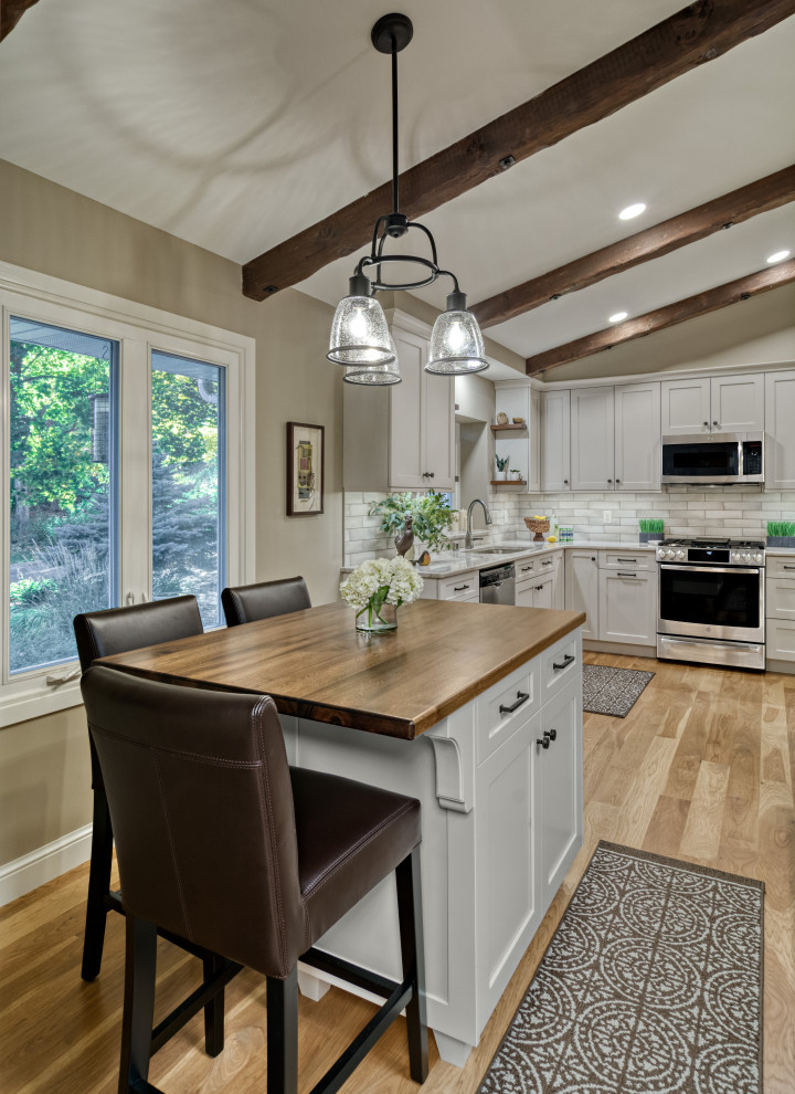 Design ideas for a mid-sized traditional l-shaped eat-in kitchen in Minneapolis with an undermount sink, flat-panel cabinets, white cabinets, white splashback, ceramic splashback, stainless steel appliances, with island, brown floor and white benchtop.
