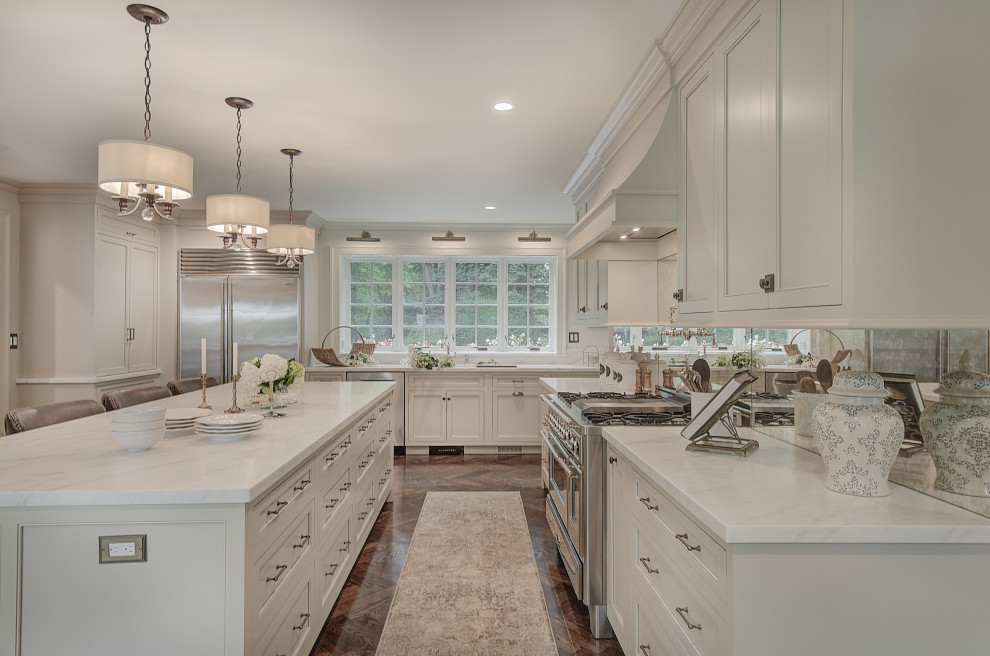 Design ideas for an expansive traditional u-shaped kitchen in New York with an undermount sink, beaded inset cabinets, beige cabinets, marble benchtops, mirror splashback, stainless steel appliances, medium hardwood floors, with island, brown floor and white benchtop.