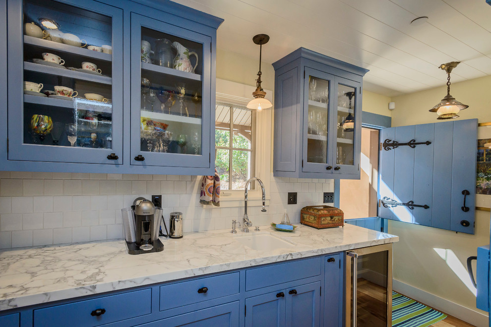Inspiration for a mid-sized country l-shaped open plan kitchen in San Francisco with blue cabinets, marble benchtops, white splashback, subway tile splashback, medium hardwood floors, a farmhouse sink, shaker cabinets, stainless steel appliances, with island and brown floor.